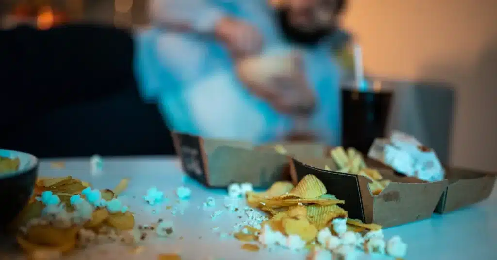 A fat man sitting in front of TV eating junk 